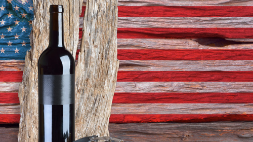 Wine bottle with a dark label rests against weathered wood, set against a rustic American flag backdrop.
