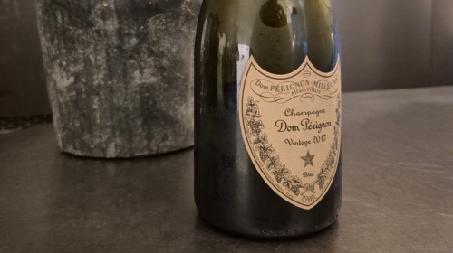 Dom Pérignon champagne bottle, Vintage 2017, on a dark counter with a metallic ice bucket in the background